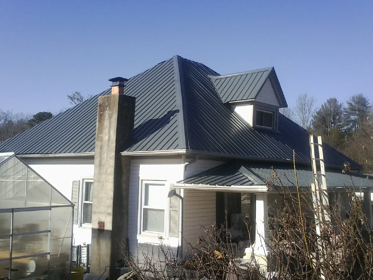 Dark blue standing seam metal roof on a white farmhouse with dormer — Slate & Tile Roof Repair by Roofing Brothers in Meansville