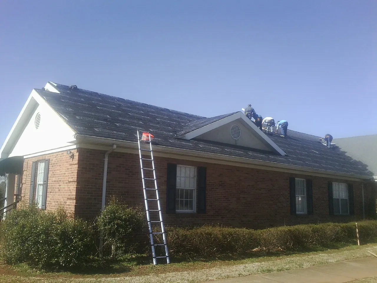 Crew tearing shingles off a brick ranch roof with a ladder set — Emergency Roof Repair work by our crew in Meansville