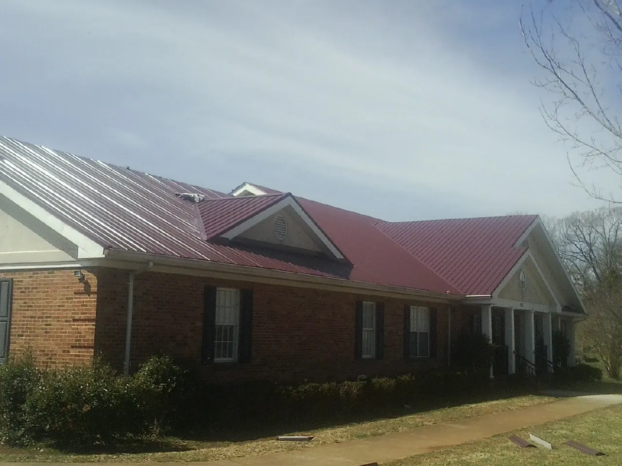 Red metal roof with gabled entries on a long brick building, from a Hail Damage Roof Repair job in Meansville