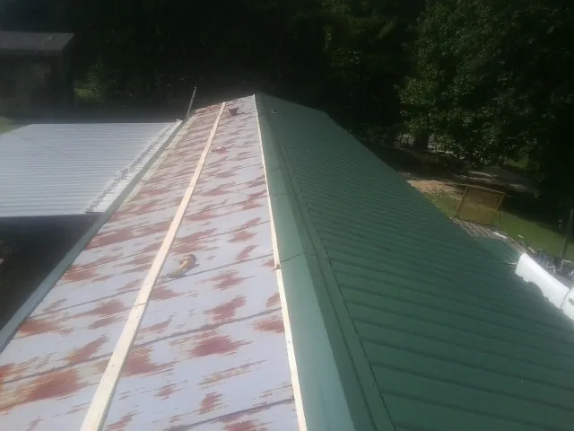 Old rusted panels beside newly installed green metal roofing — Wind Damage Roof Repair by Roofing Brothers in Meansville