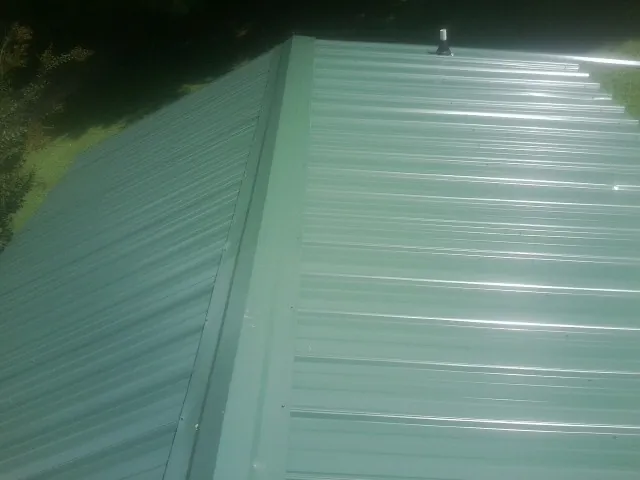 New green metal panels meeting at the ridge of a roof — Flat Roof Repair work by our crew in Meansville