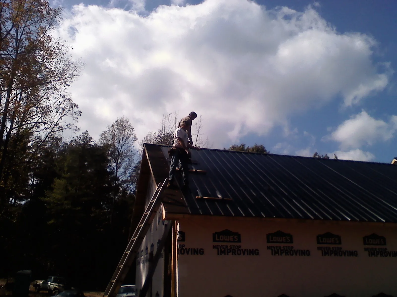 Roofer fastening dark metal panels high against a cloudy sky, from a Roof Inspection job in Meansville