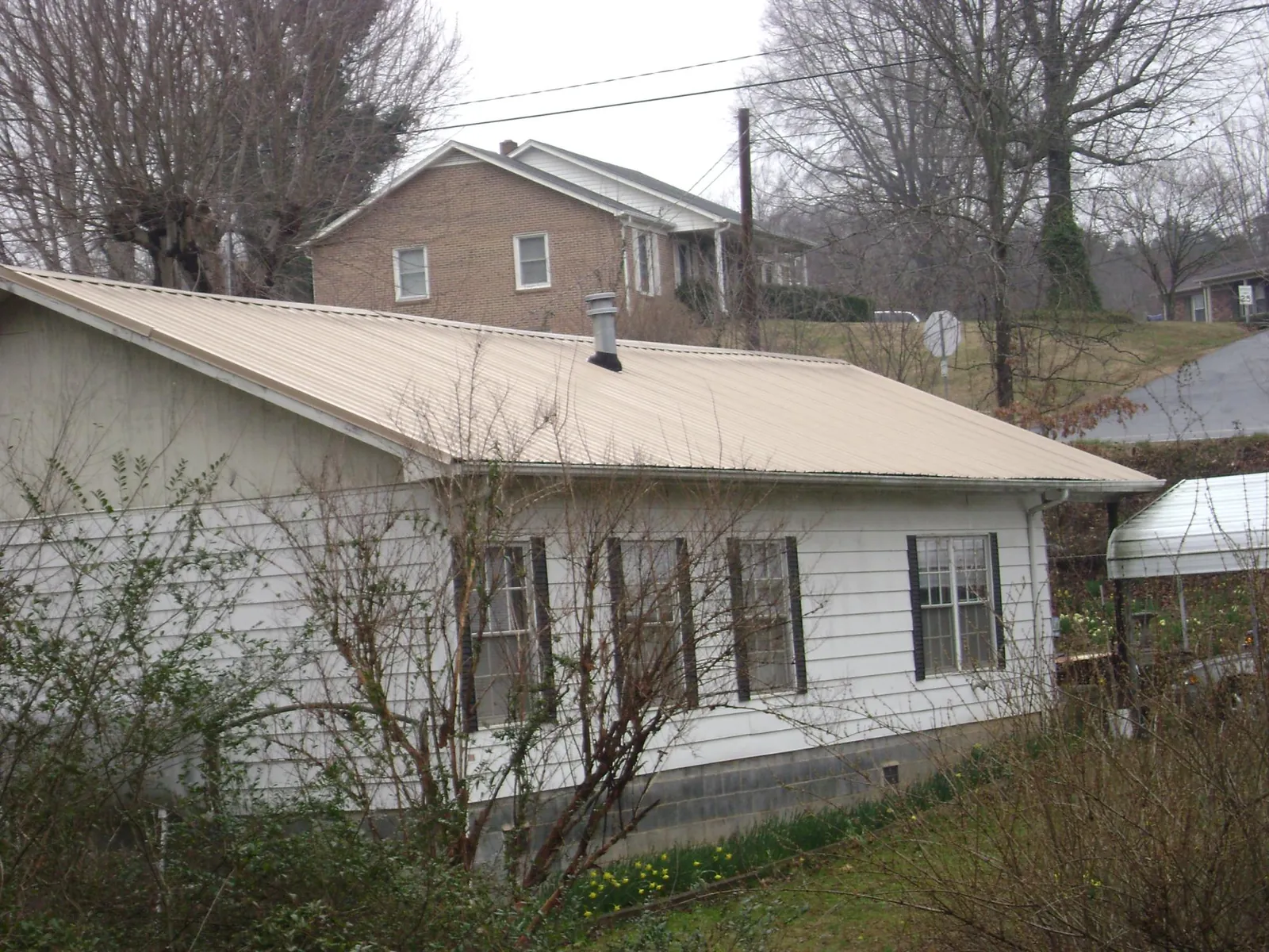 Tan metal roof on a white sided house set into a hillside — Commercial Roofing by Roofing Brothers in Meansville