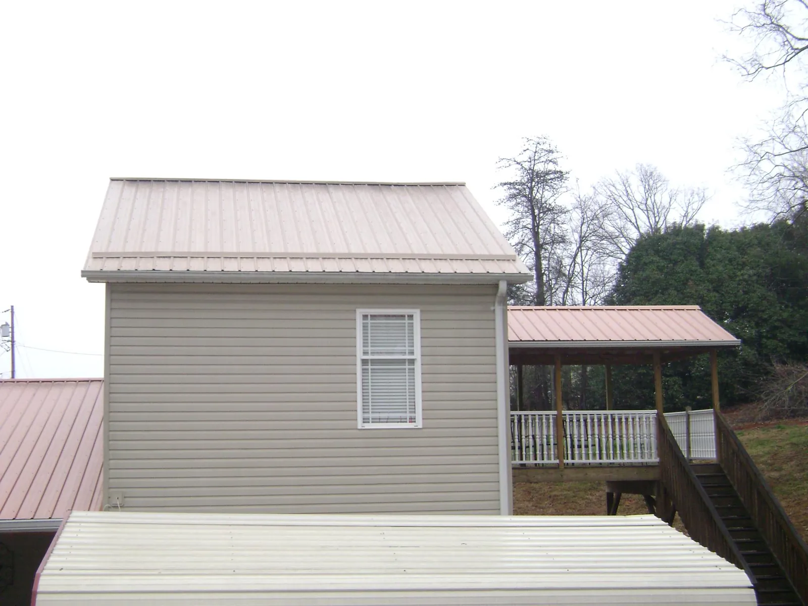 Tan metal roofs on a two story addition and attached porch, from a Roof Replacement job in Meansville
